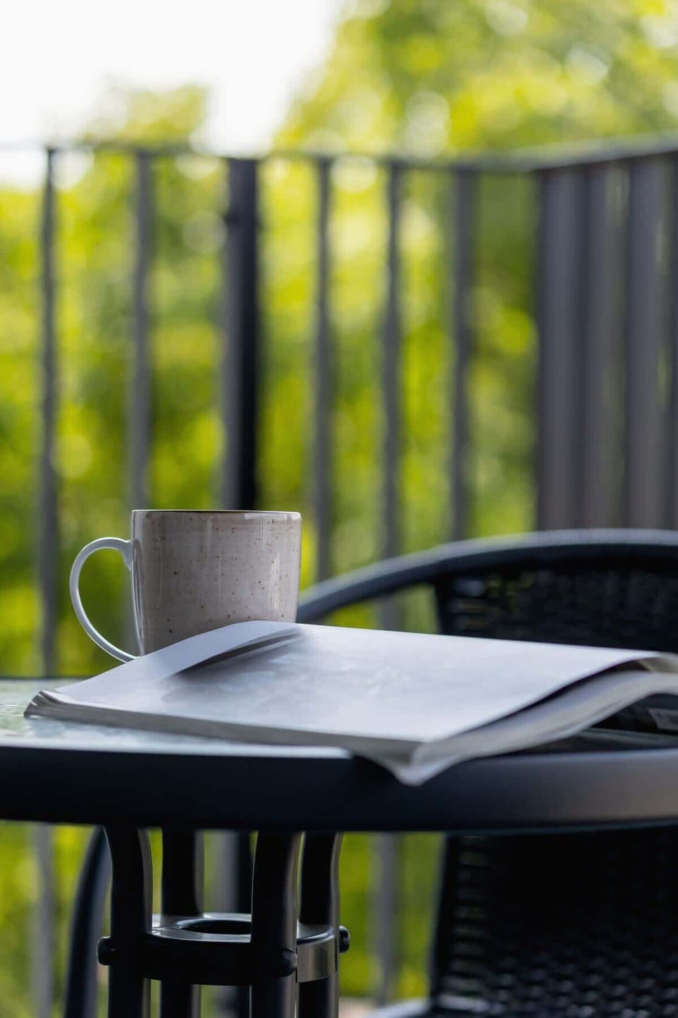 A close-up of a balcony railing with a coffee cup, overlooking a peaceful and green environment.
