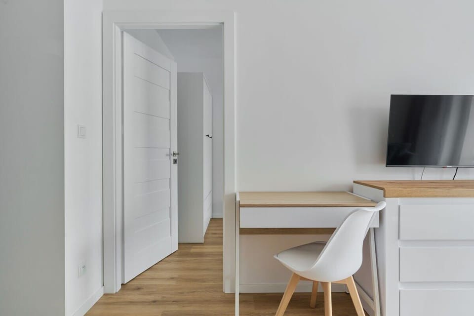 A bright work space with white chairs and a wooden table, leading to the kitchen area.
