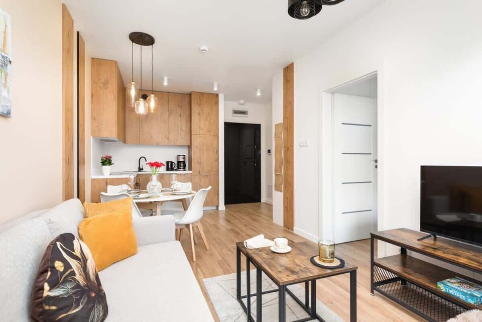 A living room with a sofa, bright cushions, and an open-plan layout connecting to the kitchen.
