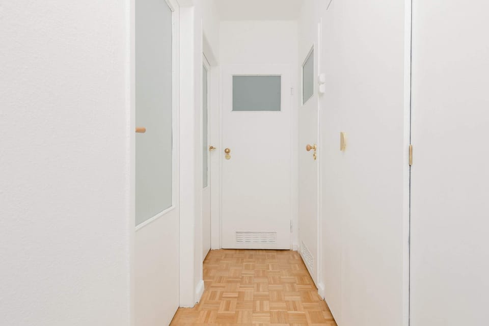 A bright, minimalist hallway with parquet flooring and white doors, creating a clean and inviting entrance to the apartment.






