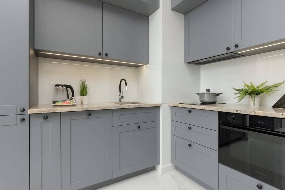 A contemporary kitchen in gray tones, equipped with modern appliances, white countertops, and minimalist decor.


