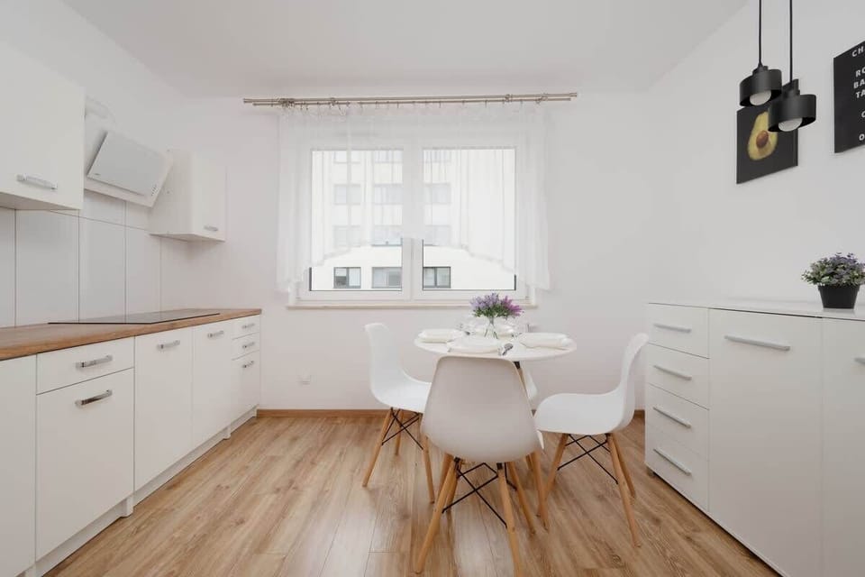 A bright kitchen with white cabinetry, a small dining area, and natural light streaming in through the window.

