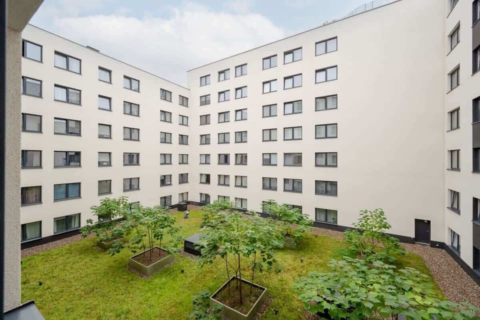 An inner courtyard of a residential building, featuring a landscaped green area with plants, pathways, and seating benches for relaxation.
