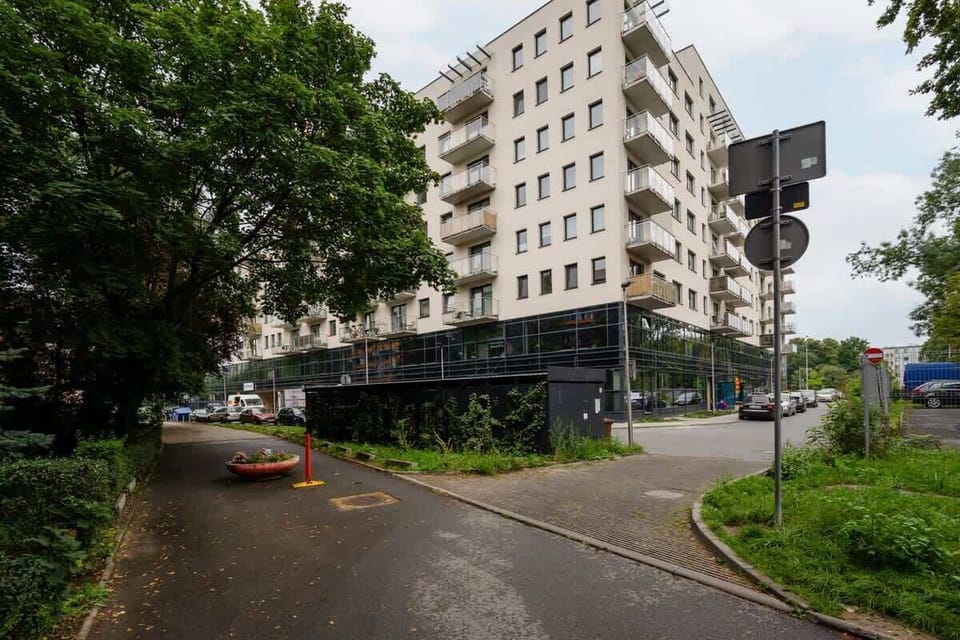 An exterior view of the residential building, surrounded by greenery, a paved driveway, and a well-maintained garden.

