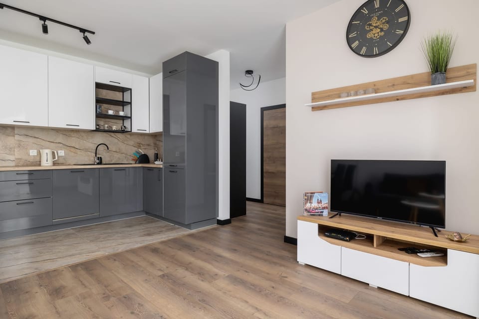 An open-plan kitchen and living area with light wooden flooring, a sleek TV stand, and modern cabinets in neutral tones.

