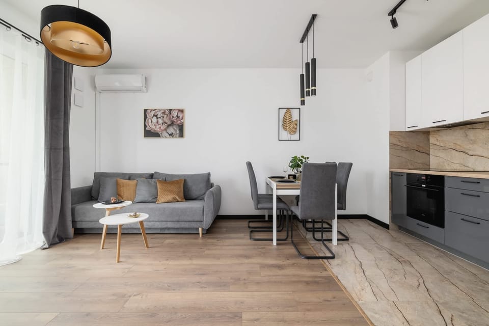 A living and dining area from another angle, showing the gray sofa, a wooden floor, and the seamless connection to the kitchen.

