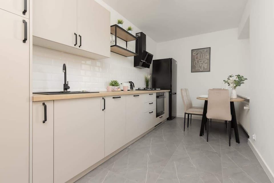 A minimalist kitchen with white cabinets, black fixtures, and a tiled floor, offering a clean and modern workspace.

