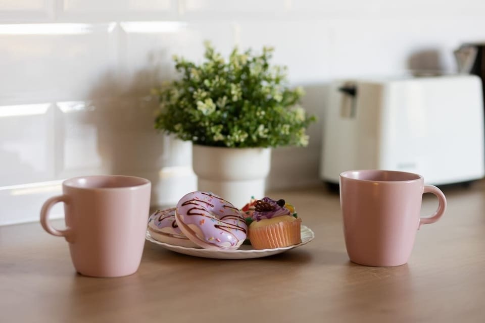A close-up of a kitchen counter with coffee mugs, fresh pastries, and a small plant, adding a welcoming touch to the space.

