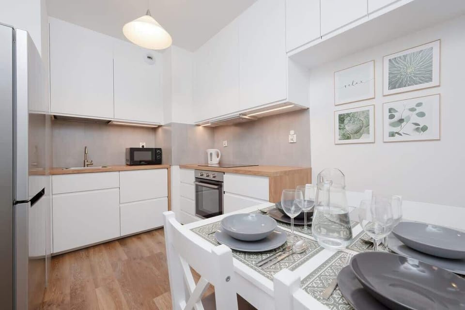 A compact kitchen with white cabinets, wooden countertops, and a neatly set dining table, blending style and practicality.

