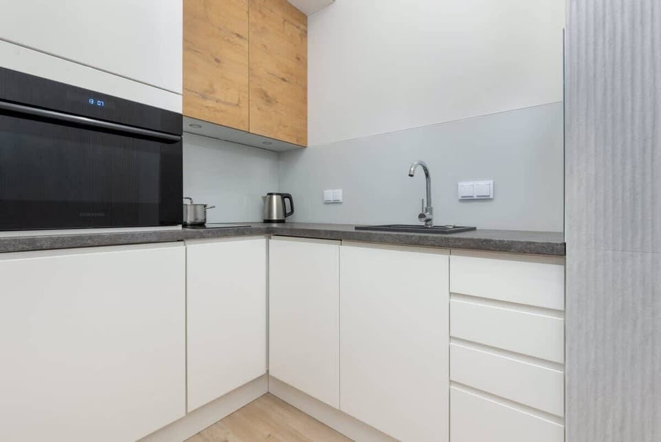 A minimalist kitchen with white cabinets, wooden upper shelves, and integrated appliances, combining simplicity and elegance.

