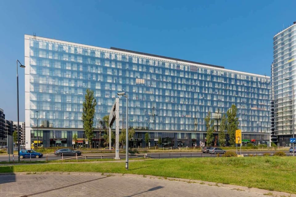 The exterior of a modern building with a glass facade, surrounded by greenery and a clean urban environment.

