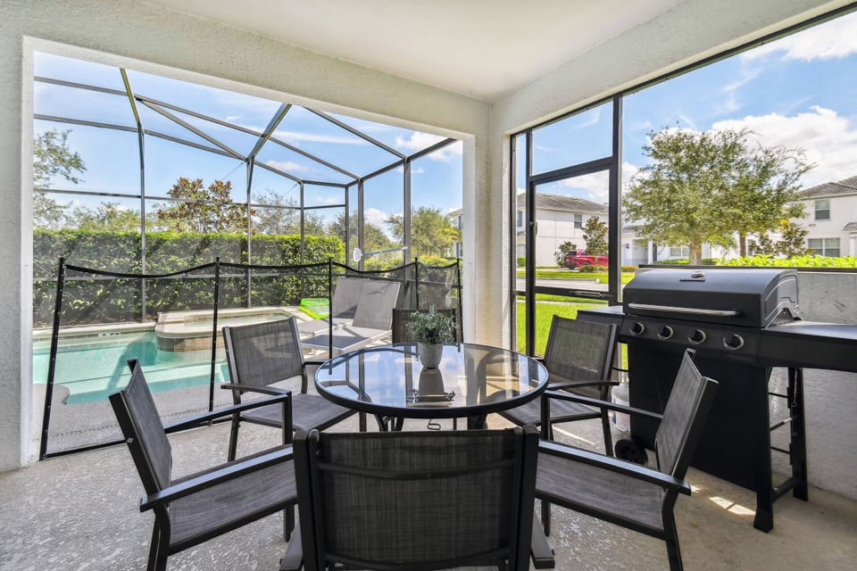 Relax in a bright screened-in patio filled with natural light, featuring a stylish black table for six. Enjoy dining al fresco with views of the inviting pool and lush greenery, plus a convenient grill for your cookout plans.