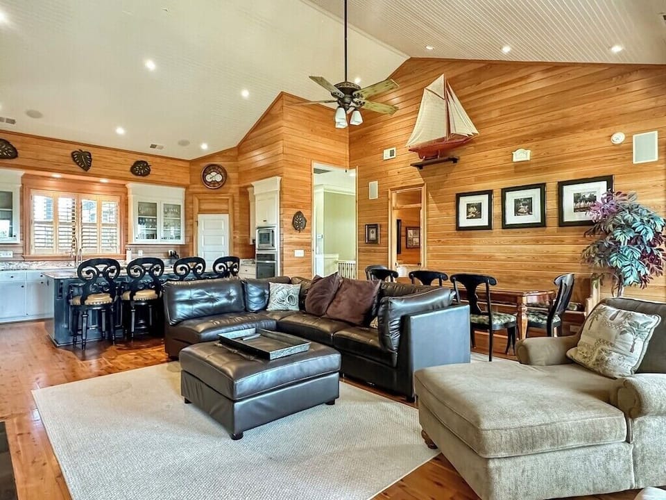An open-concept family room and dining room with warm wood paneling, trim work, high ceilings, and a ceiling fan.