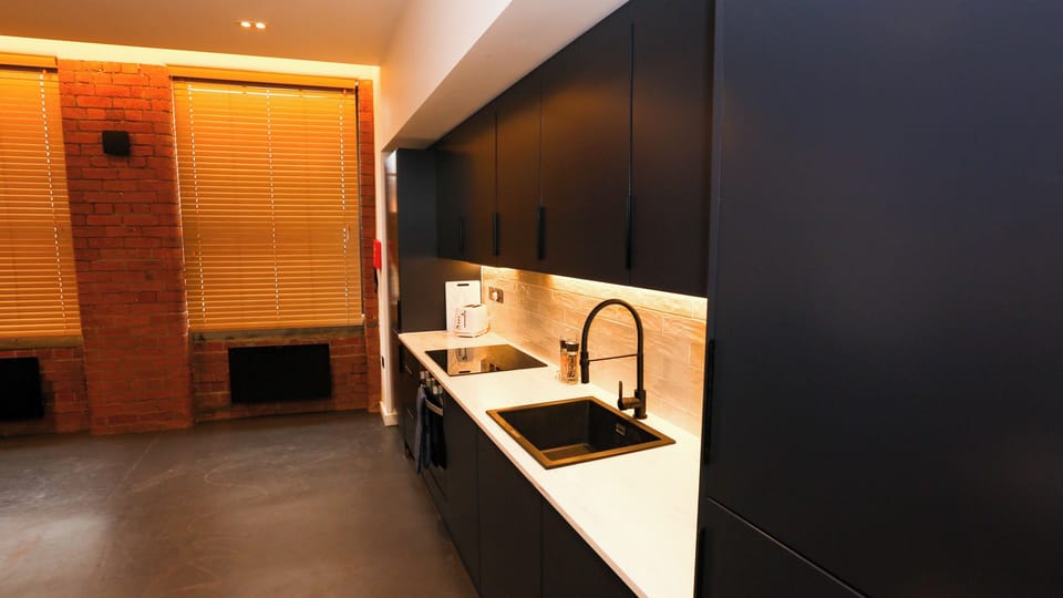 Contemporary kitchen with black cabinets, integrated oven, sink, red brick feature wall – The Nichols Bldg, Sheffield