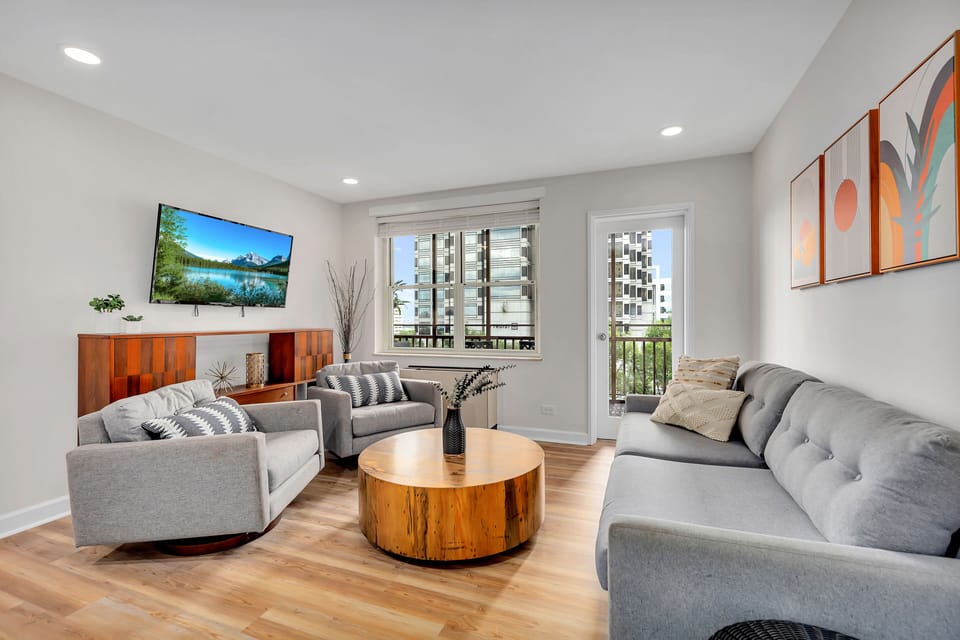Bright living room w/ cozy seating, wood coffee table & large windows bringing in natural light