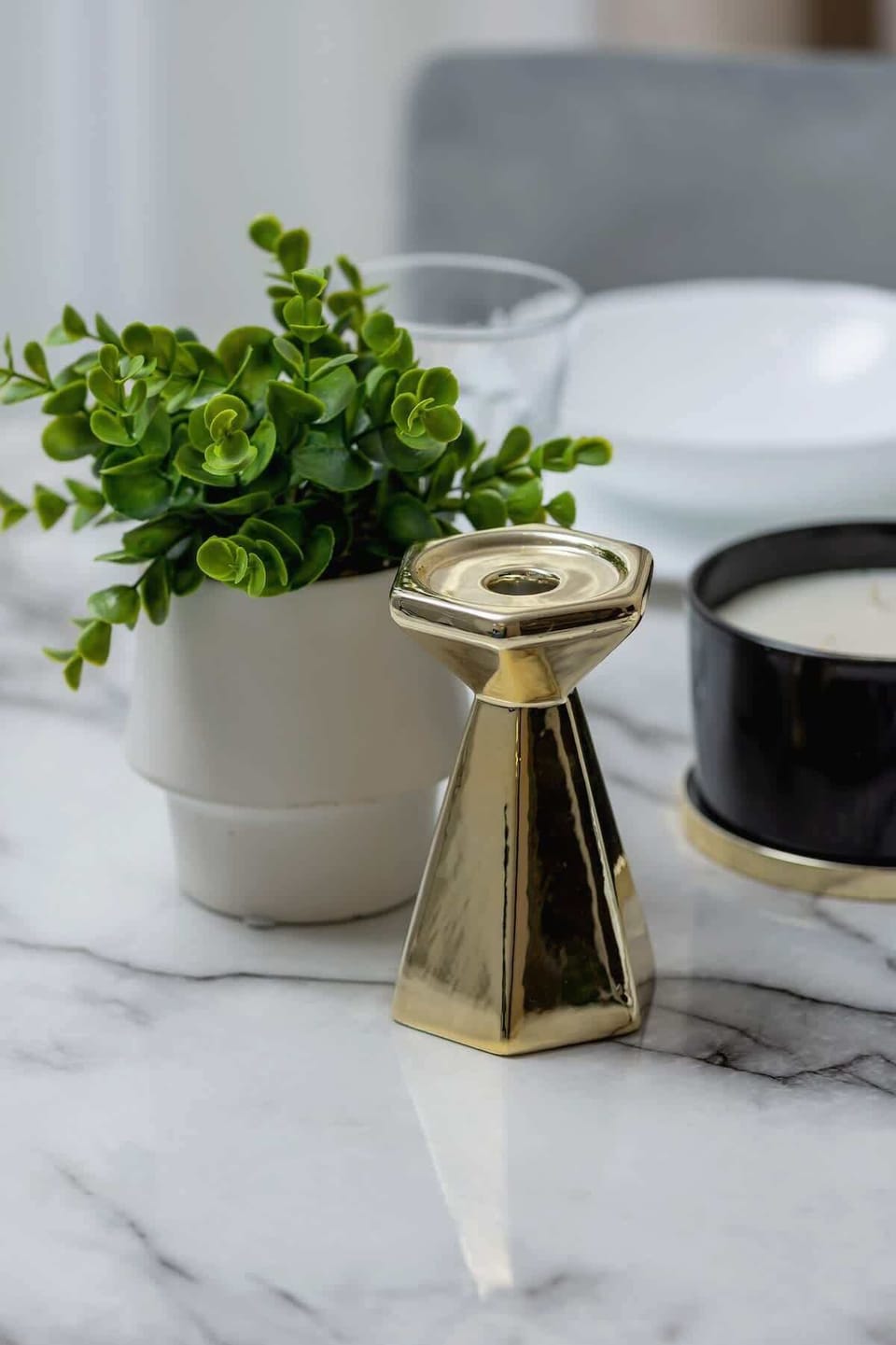A marble surface adorned with a gold jug, a small potted plant, and black cups, adding an elegant and stylish focal point.
