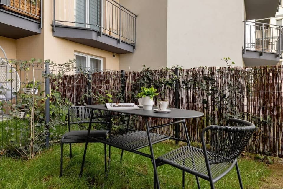 A cozy outdoor patio with a small metal table and chairs, set in a fenced grassy area, perfect for relaxation or enjoying a meal outside.
