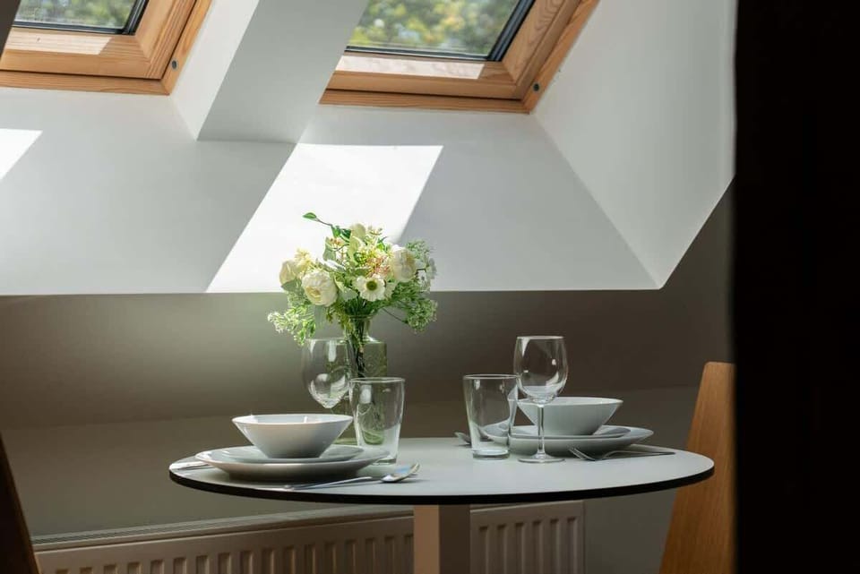A dining nook under a skylight with a small table and neatly set plates, offering a cozy and bright spot for meals.

