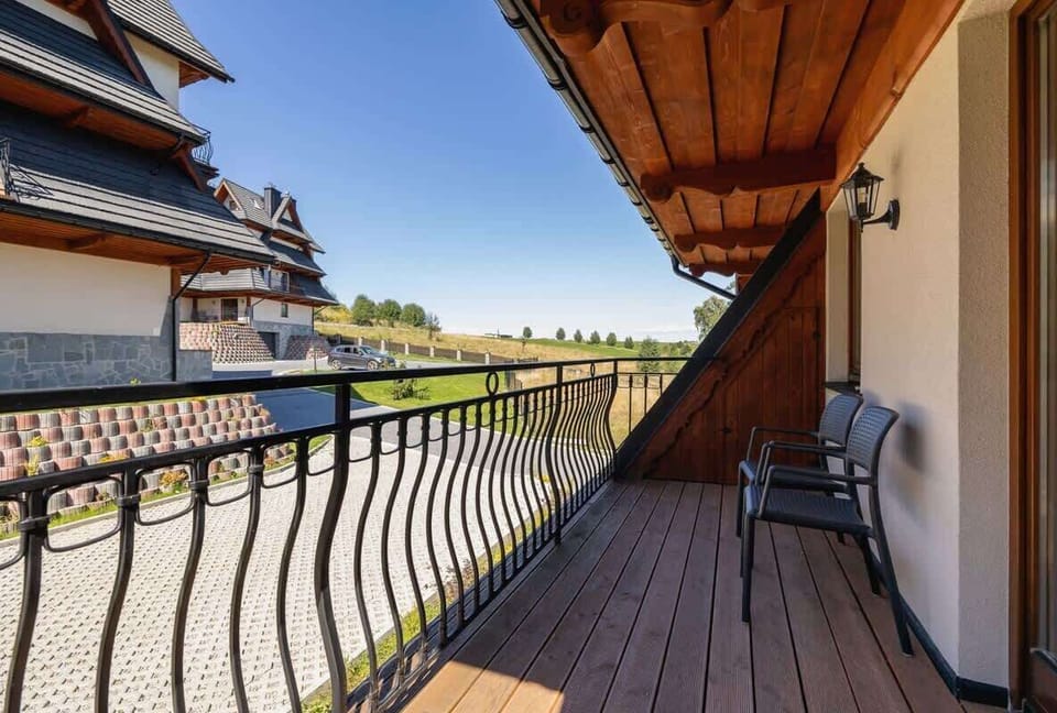 A balcony with wooden railings and a scenic view of the surroundings, equipped with chairs for relaxing outdoors.
