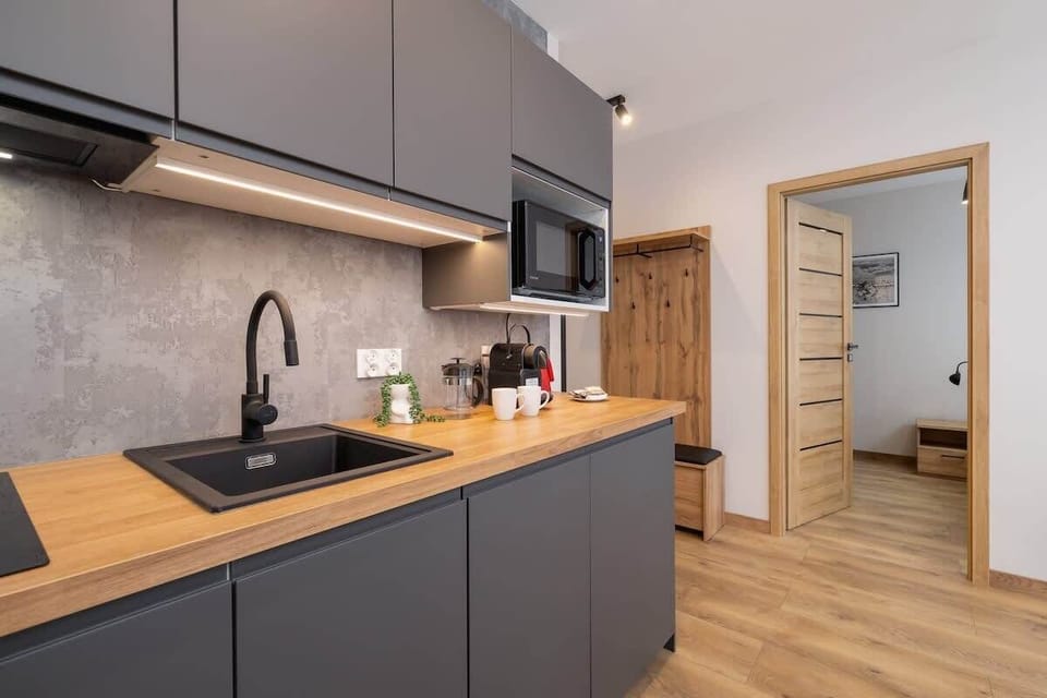 A compact kitchen with gray cabinets, black countertops, and wooden flooring, blending modern design with practicality.
