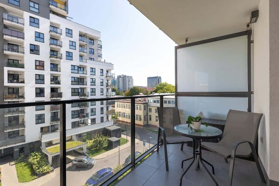 A balcony view featuring a small table and two chairs, overlooking a modern residential complex, ideal for enjoying fresh air.
