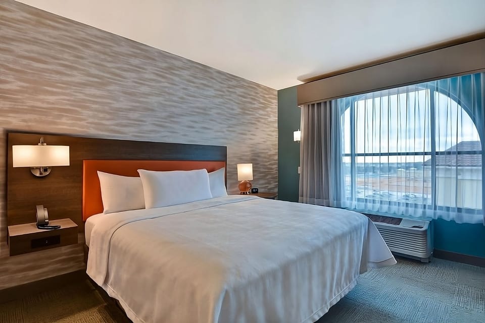 Unwind in crisp bedding beside a sunlit, arched window.