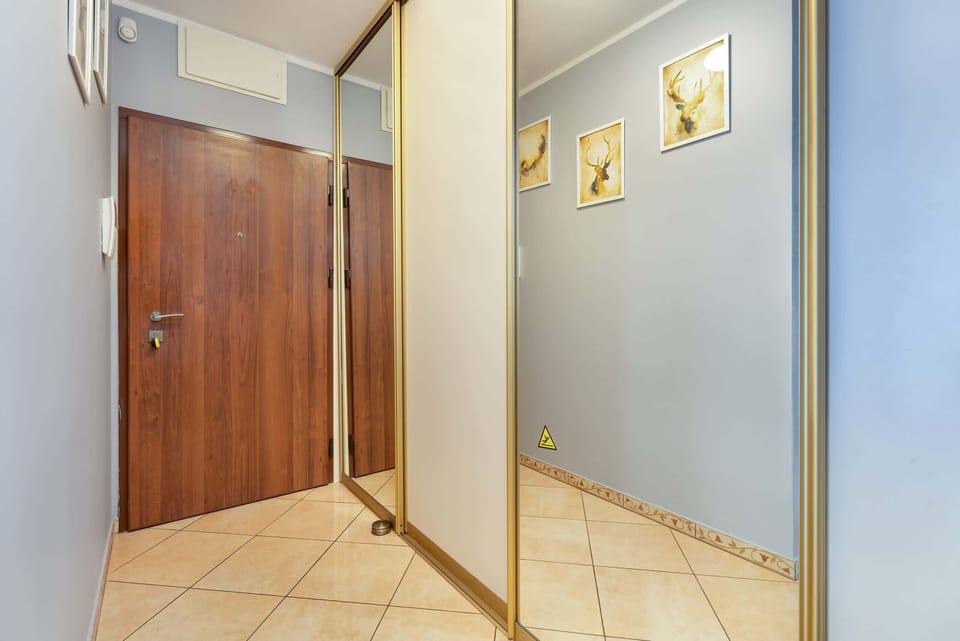 Corridor with a large mirror, elegant lighting, and a bright, playful decor style featuring a bold magenta chair.