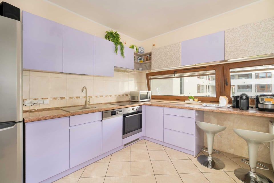 A modern kitchen with purple and beige cabinets, a sleek tiled floor, and ample counter space, creating a functional and stylish cooking area.