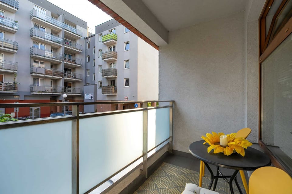 A balcony with a small table and yellow flower decorations, offering a view of nearby apartment buildings and greenery.