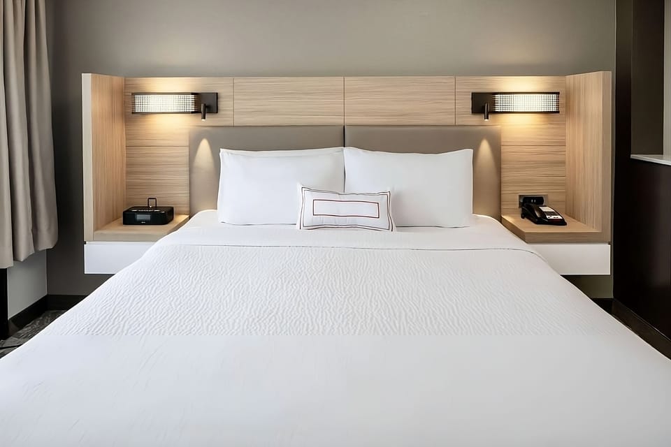 Sink into crisp linens beneath warm, calming bedside lights.