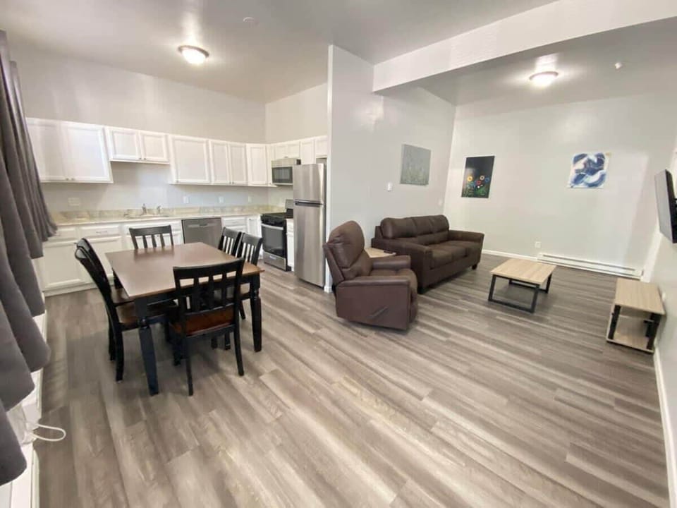 A spacious open floor plan connects the kitchen, dining, and living areas. The kitchen has modern appliances, the dining area features a sleek table and chairs, and the living room offers a plush sofa with natural light streaming through large window