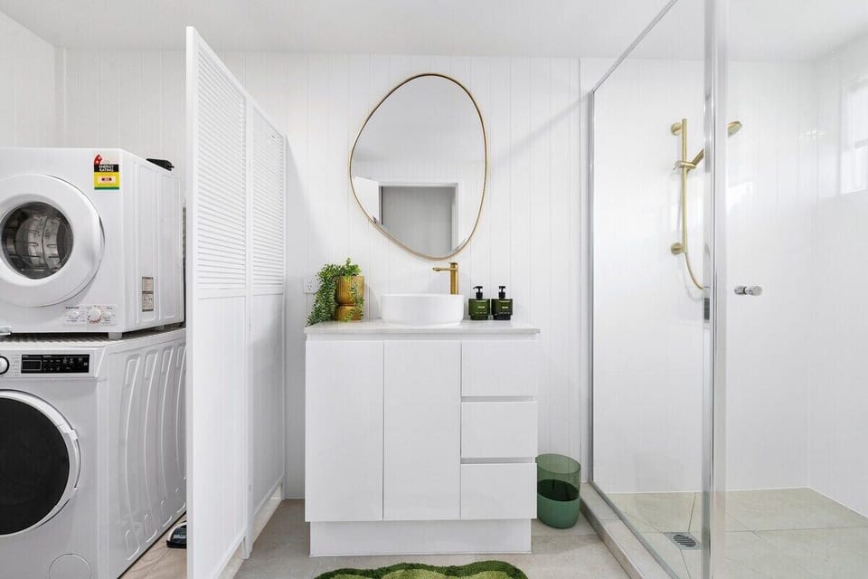Fully renovated bathroom with a shower, vanity, washer and dryer.