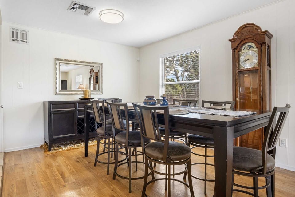 A classic formal dining room featuring a dark wood table with seating for eight, anchored by an elegant grandfather clock and a matching buffet with a large silver-framed mirror.