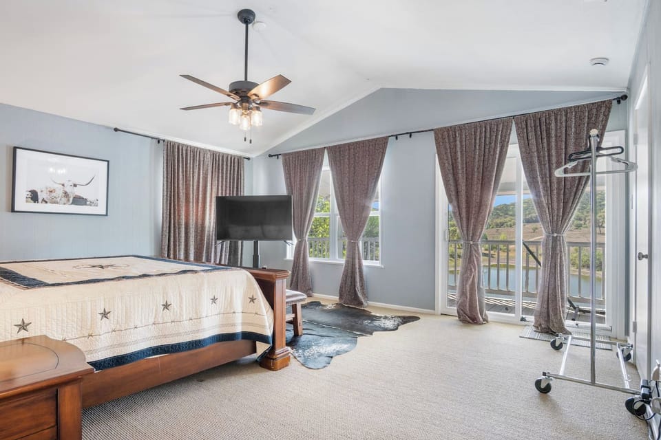 
An airy primary suite featuring vaulted ceilings and a private balcony that offers serene views of the surrounding hills and water. The room is styled with rustic accents, including a star-patterned quilt and a cowhide rug.
