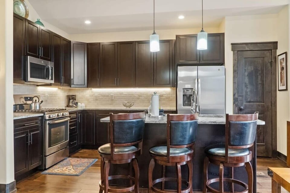 The kitchen features stainless steel appliances, spacious granite countertops, a range of basic cookware, and a kitchen island with 3 barstools.