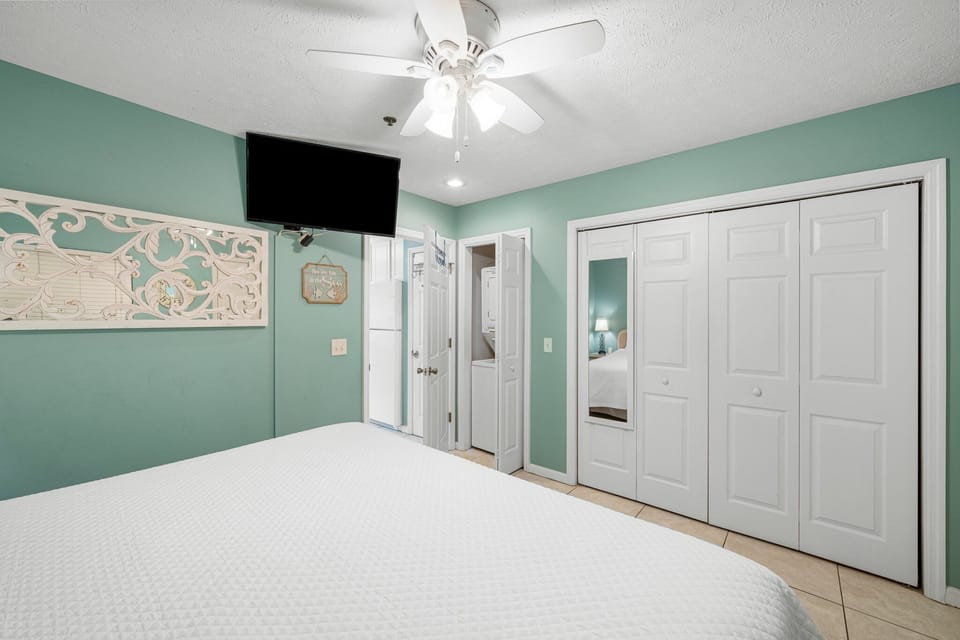 Airy primary bedroom w/ a cozy bed, ceiling fan, TV & plenty of space to settle in.