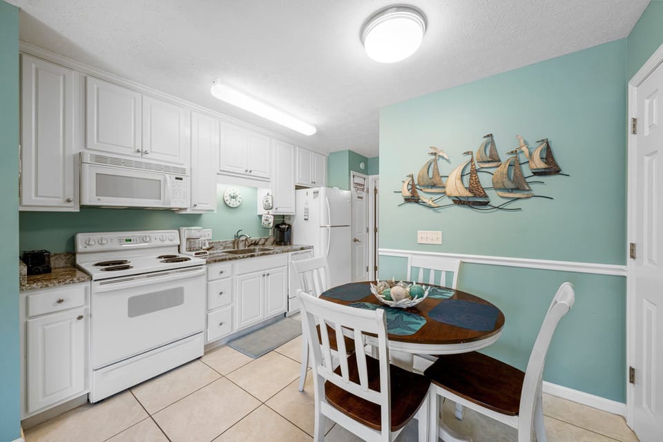 Cheerful kitchen & dining area w/ white cabinets, full appliances & a cozy table for meals.