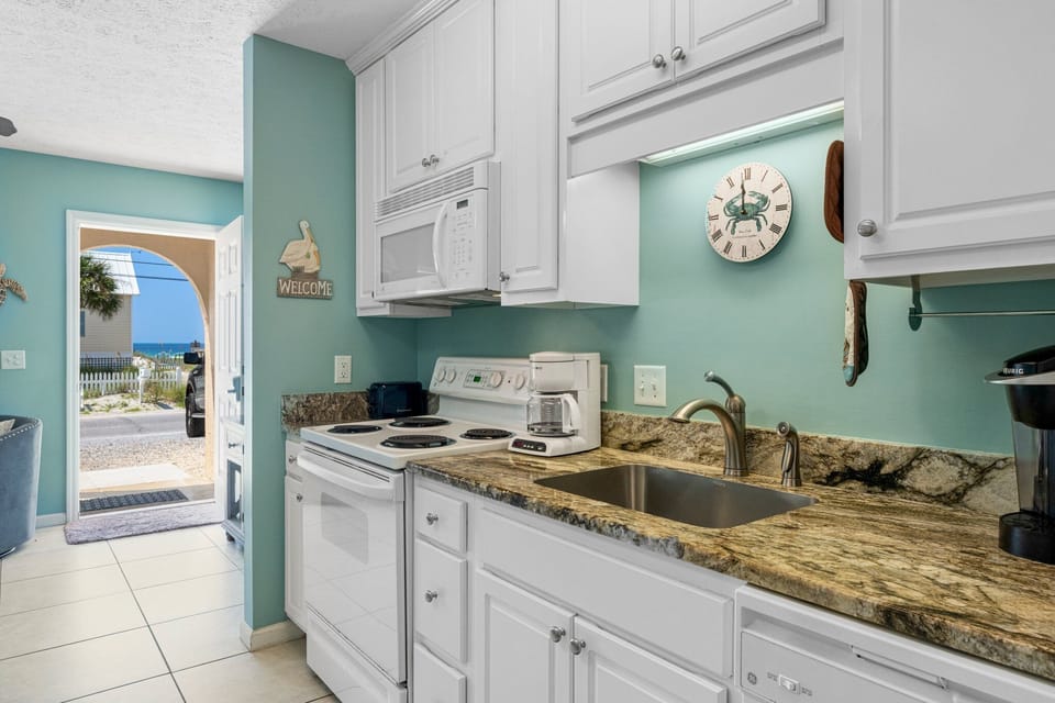 Compact kitchen w/ white cabinetry, dark countertops & everything you need to cook up a meal.