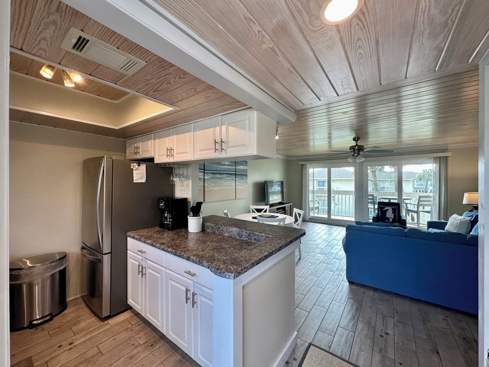 Your open-concept kitchen flows seamlessly into the living area, featuring granite countertops and stainless steel appliances under charming wood-beamed ceilings.