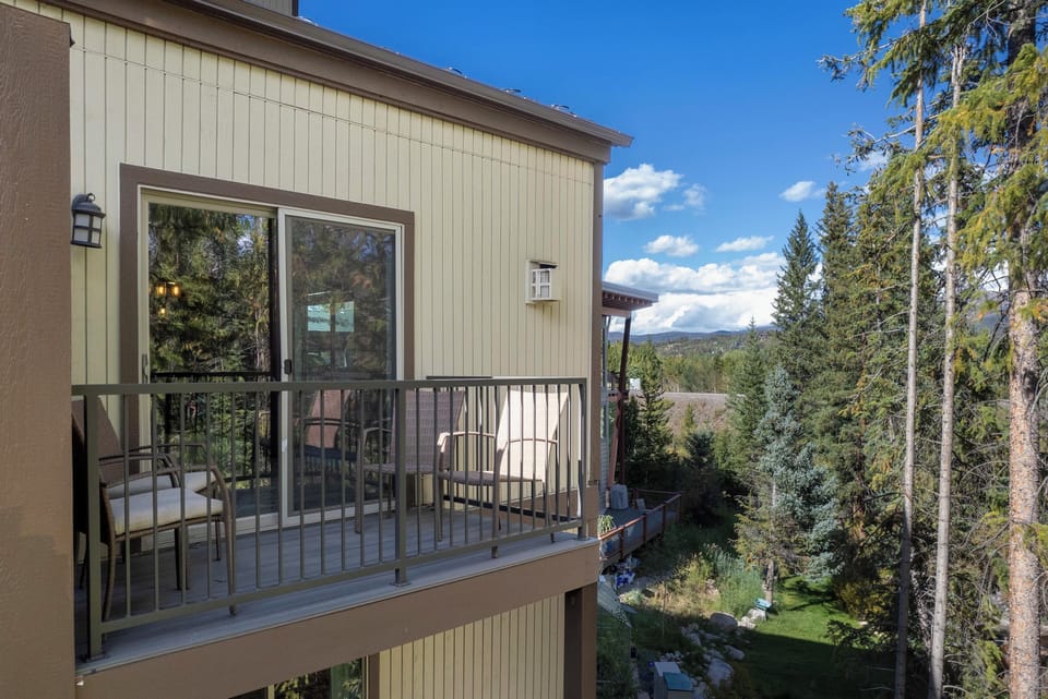 Modern mountain retreat with elevated deck overlooking forested valley and distant peaks under clear blue skies.