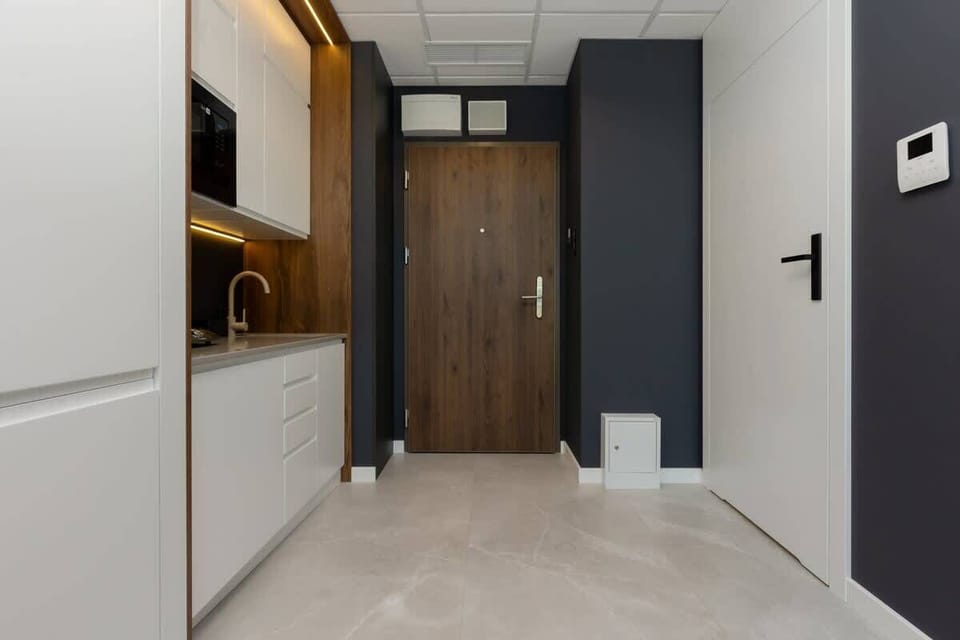 A hallway with light-colored flooring, a wooden accent wall, and sleek white cabinetry, designed with modern minimalism in mind.
