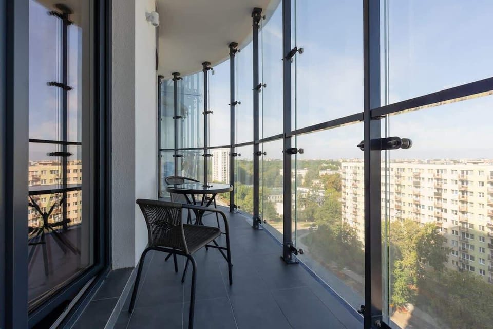 A balcony with a glass enclosure, offering a modern seating area and a view of the surrounding cityscape.
