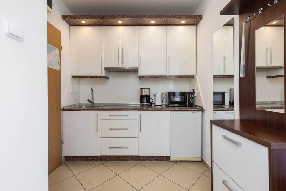 A compact kitchen with white cabinets, tiled floors, and modern appliances, designed for practicality and style.

