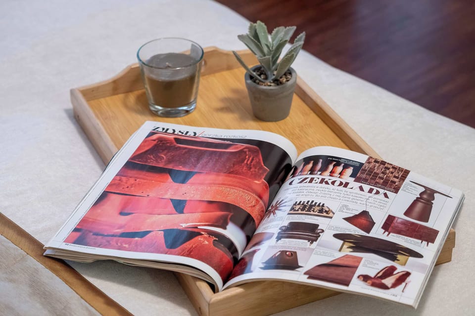 A close-up view of an open book placed on a wooden table. A small plant and a cup sit nearby, adding a relaxing and homely touch.