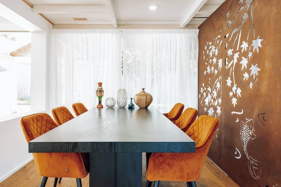 Gather in the dining area, adorned with comfortable seating for six, accented with vibrant orange touches, creating a warm and inviting atmosphere.