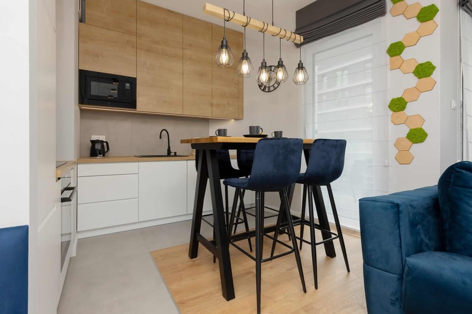 Another view of the kitchen featuring a dining area with black chairs, pendant lighting, and wooden finishes.
