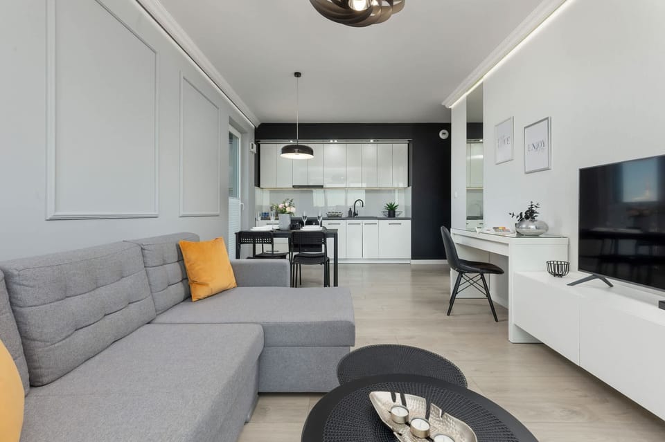 A modern living area featuring a gray sofa, yellow accents, and a mounted TV on a white entertainment unit.

