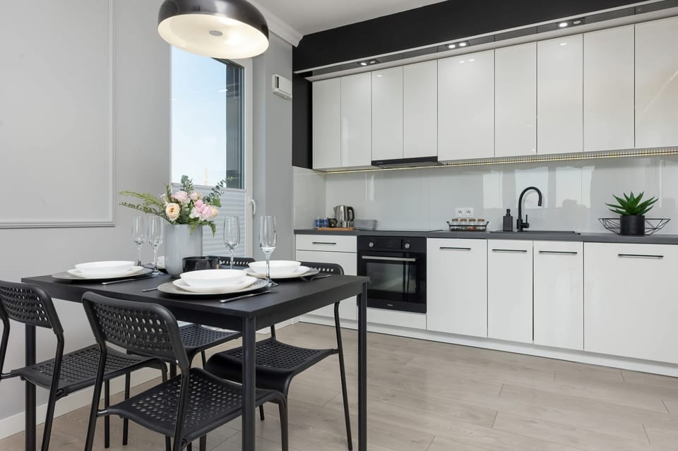 A sleek kitchen with white cabinets, black countertops, and a dining table with black chairs, blending elegance and functionality.
