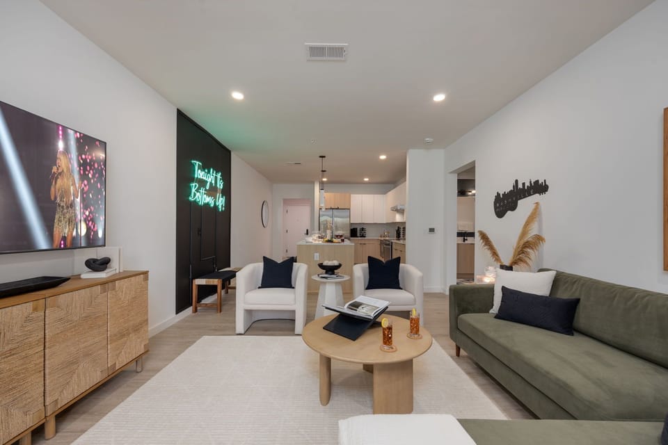 Spacious living area with ample seating, designer decor, smart TV, board games, printer, and sliding glass door to the shared communal areas including a sparkling blue pool.