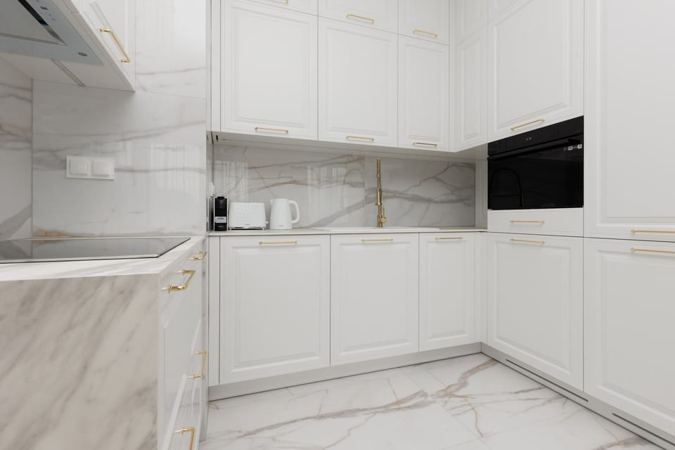 A modern kitchen with white cabinetry, marble countertops, and integrated appliances.


